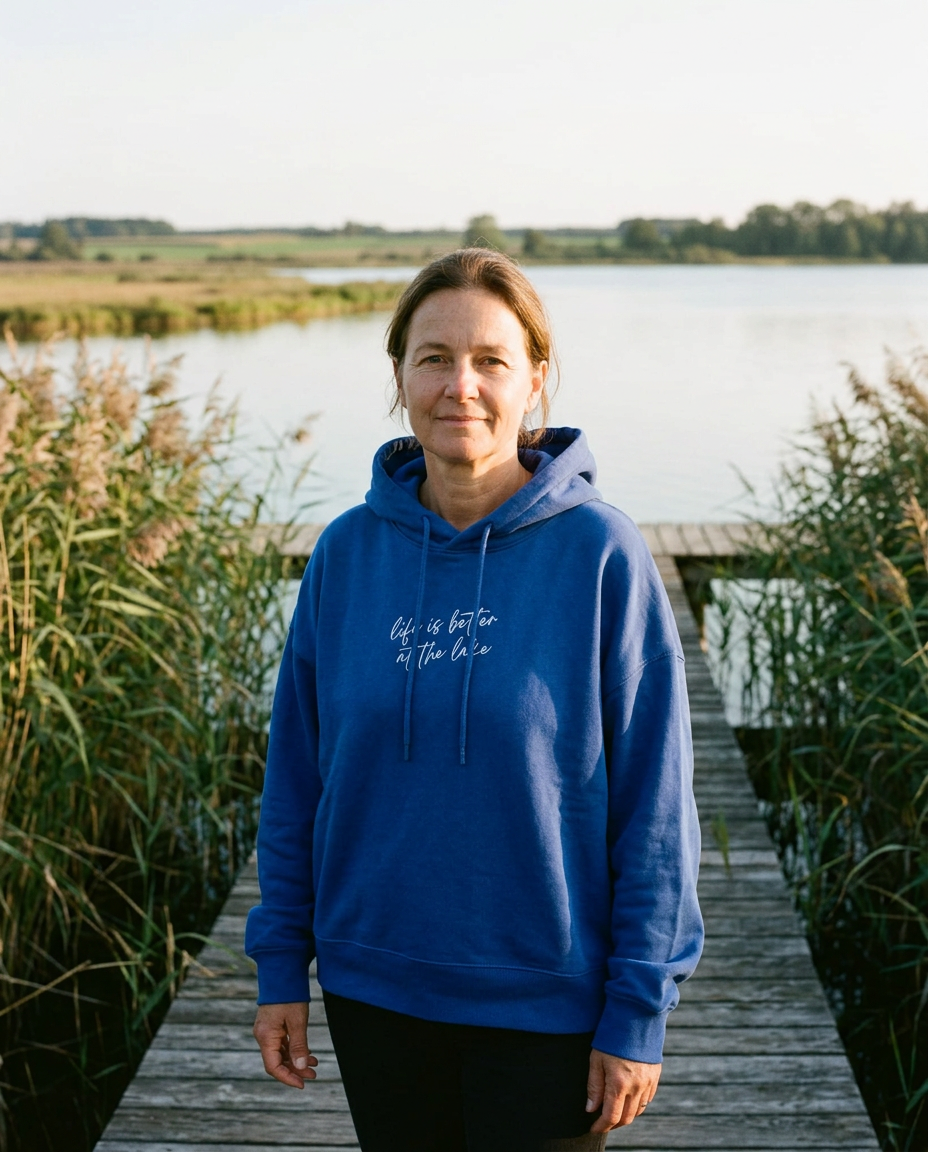 Blauer SEEVIBES Hoodie mit weißem Druck „life is better at the lake“ am Holzsteg getragen